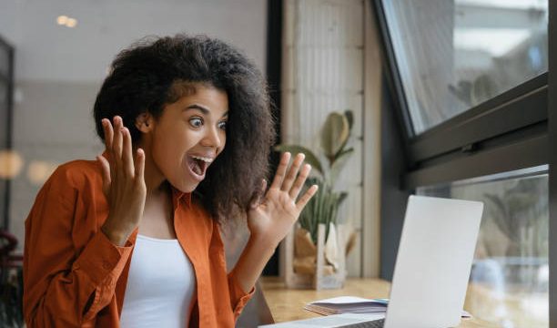 Young Excited African American woman win online lottery, celebration success. Happy emotional female using laptop computer shopping online